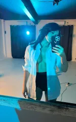Ruth taking a selfie in the mirror while wearing a white shirt unbuttoned 