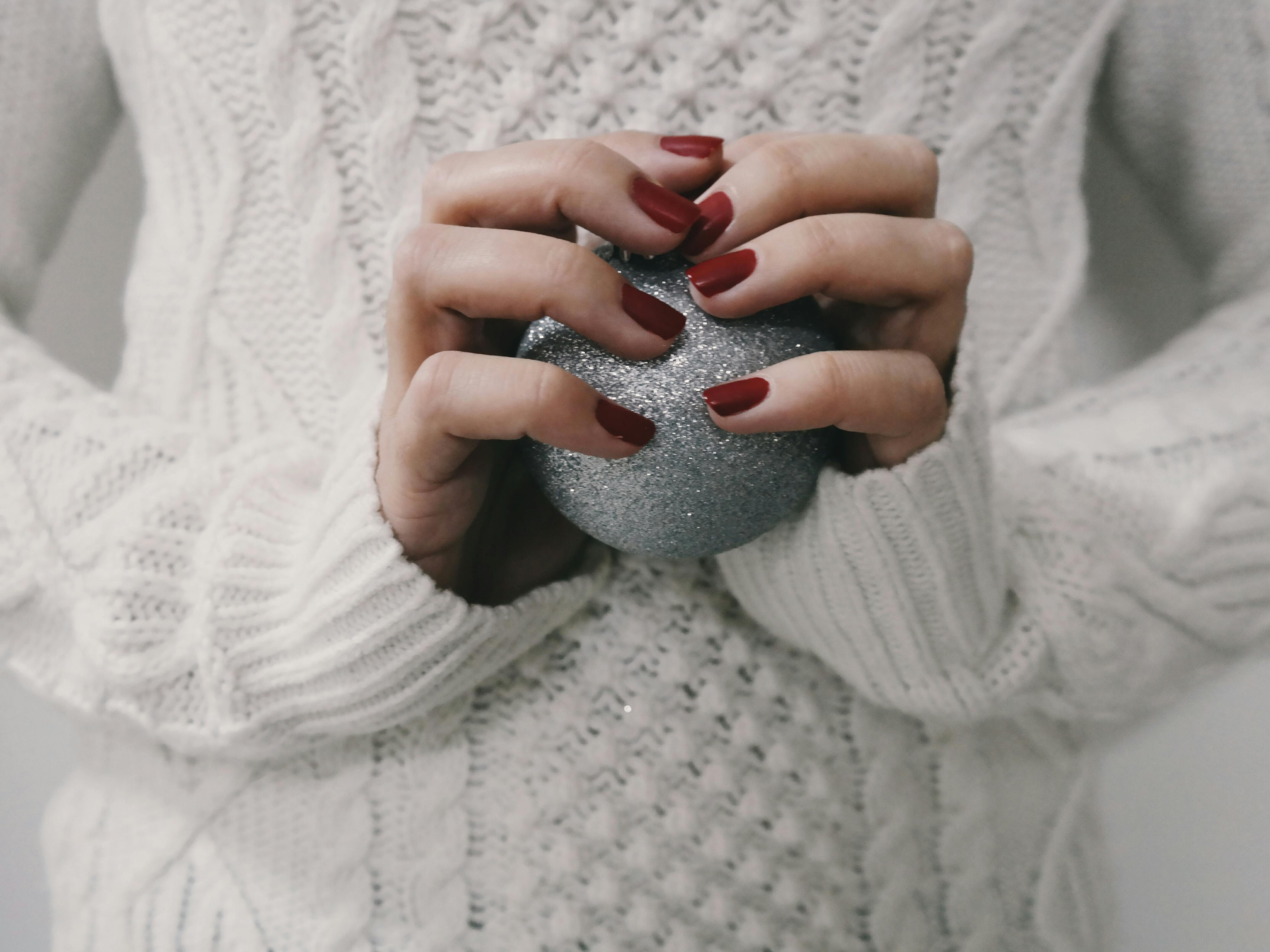 woman in a white sweater holding a glittery silver ornament